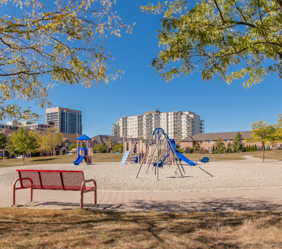 gravel park with red bench, slide, swings. buildings in background